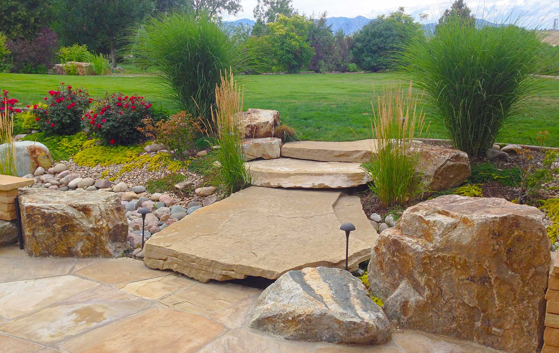 Flagstone bridge with accent boulders in Rustic Outdoor Living in Arvada Mile High Landscaping in Denver